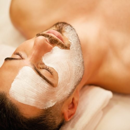 Close-up of man with white facial mask relaxing during treatment at beauty spa.